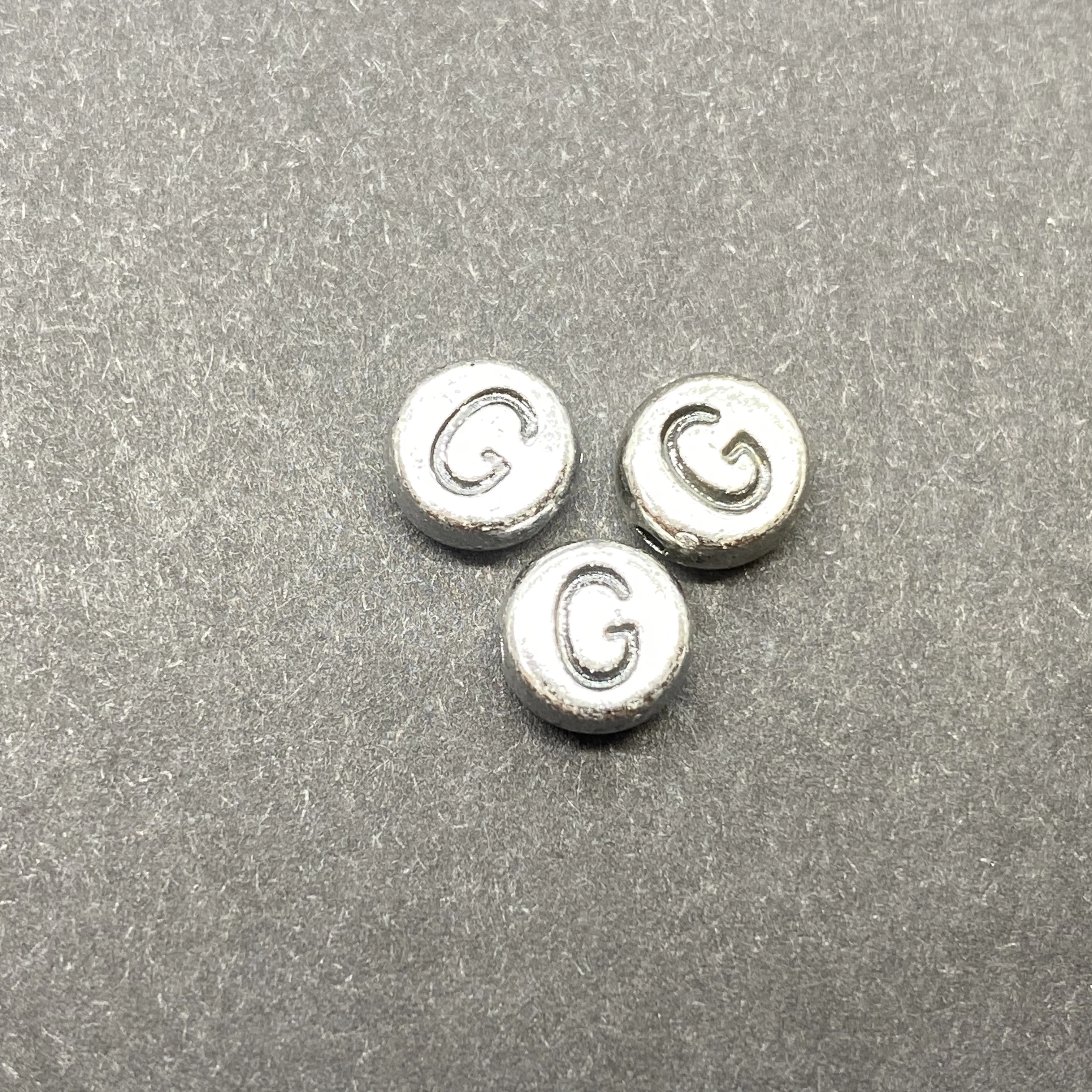Műanyag ezüst színű kör g betűgyöngy (7mm)